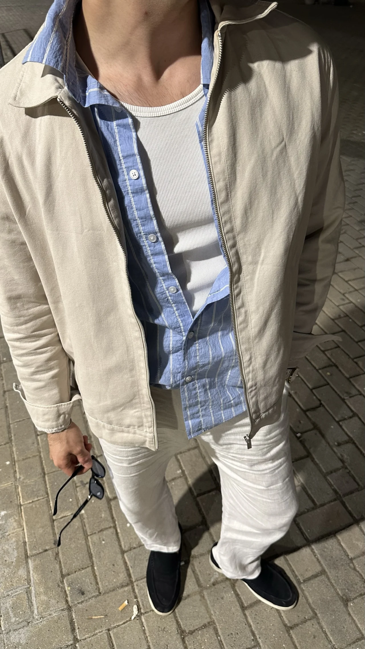 Beyaz tişört, mavi çizgili gömlek ve açık renk ceketle katmanlı bir kombin